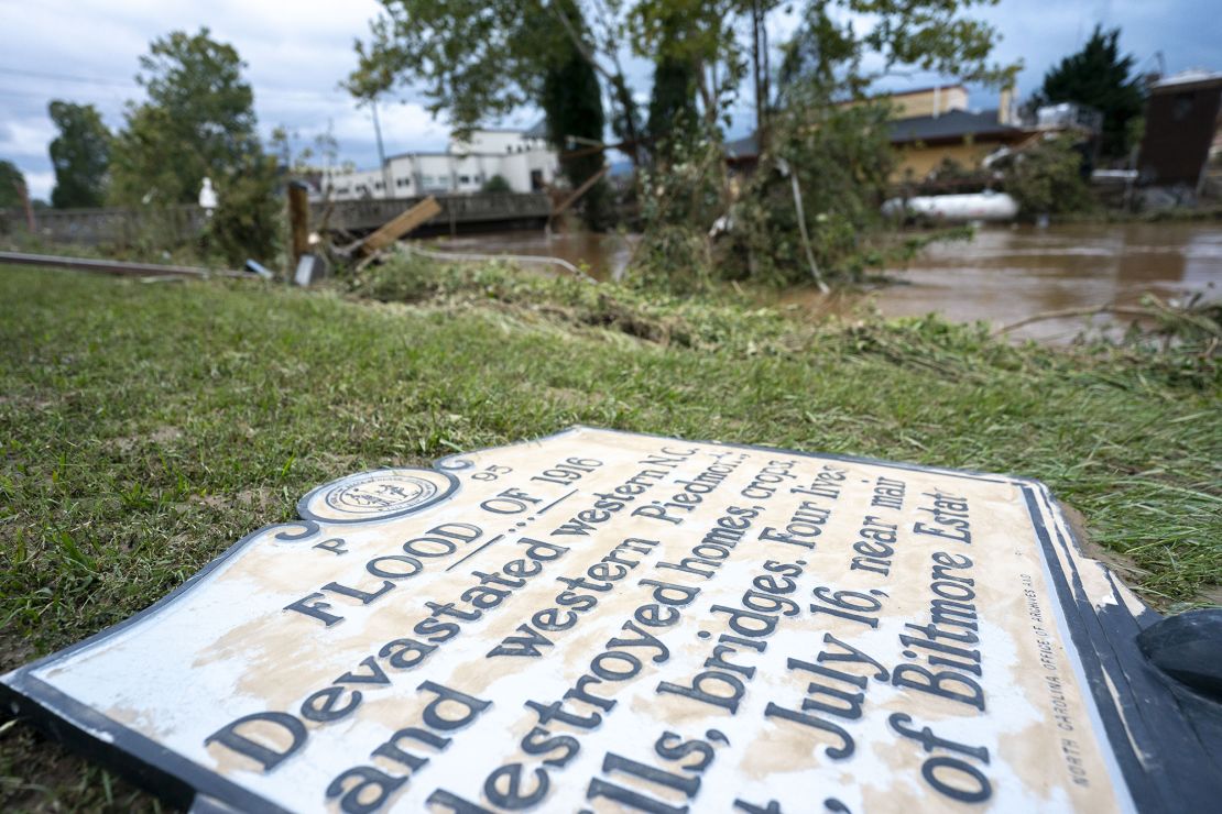 A sign commemorating the flood of 1916 lies on the ground next to a flooded waterway near Biltmore Village.