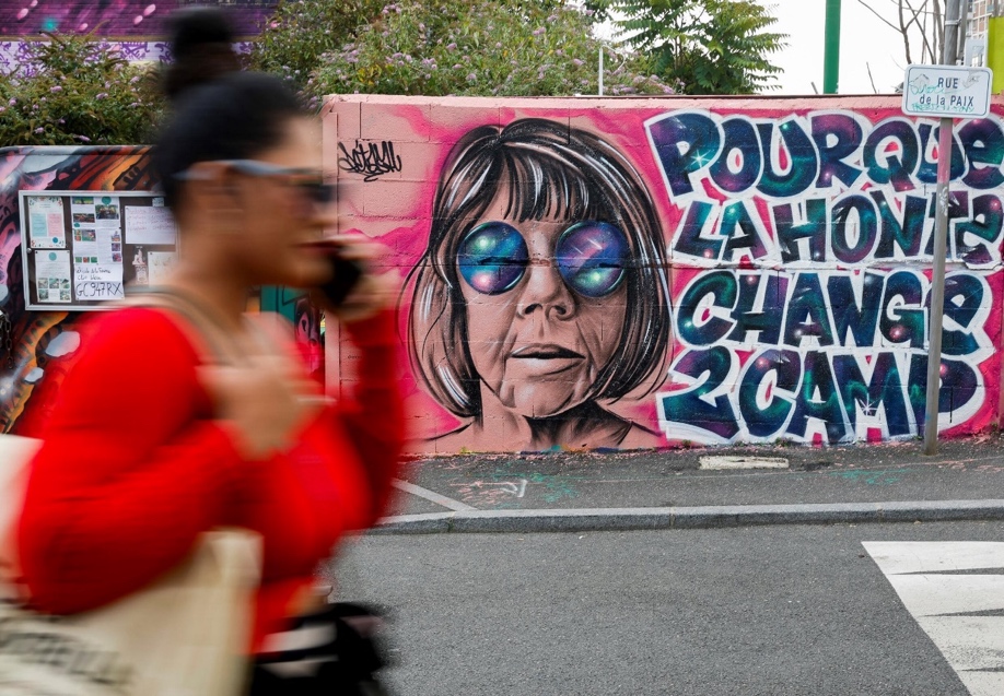 A woman walks past a mural created by Maca_dessine depicting Gisele Pelicot and a sentence reading "So that shame changes sides" in Gentilly, south of Paris on September 21, 2024 as her former partner