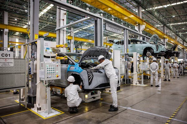 People wearing white uniforms inspecting vehicles at a manufacturing plant.