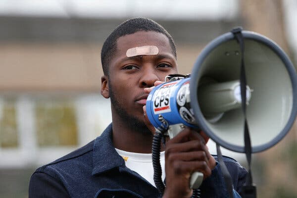 A man with a bandage on his forehead speaks into a megaphone.