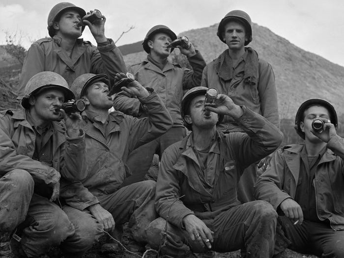 A group of US soldiers wearing helmets and fatigues drinking Coca Cola in Italy