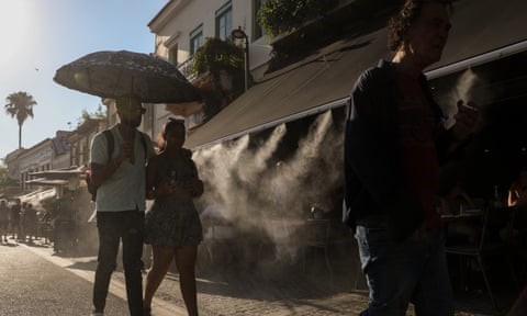 Tourists walk past a terrace with a water spray in Athens, Greece